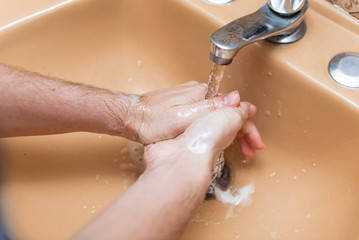Fototapeta premium Woman washing hands with soap and water in a yellow sink at home to prevent COVID-19 spread