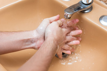 Fototapeta premium Woman washing hands with soap and water in a yellow sink at home to prevent COVID-19 spread