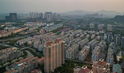 Fototapeta na wymiar Suzhou China - May 2, 2010: Aerial evening shot over many rows of gray and brown residential highrise buildings. Streets, canals and green foliage in between.