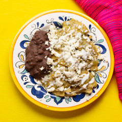 Mexican green chilaquiles with beans on yellow background