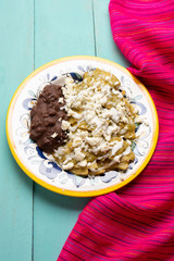 Mexican green chilaquiles with beans on turquoise background