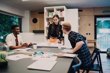 Obraz premium Progressive multiracial male and female architects developing startup design project during collaboration in modern coworking space, smart casual group of millennial brainstorming at desktop