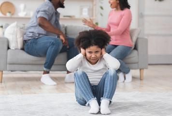 Little black girl covering ears not to listen parents arguing at home