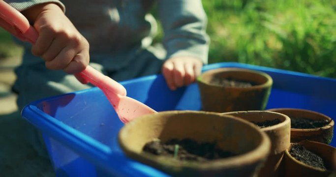 Little preschooler digging in plant pots with plastic spade