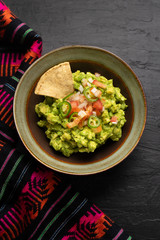 Mexican guacamole with tomato and serrano pepper on dark background