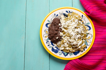 Mexican green chilaquiles with beans on turquoise background