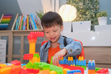 Cute little Asian kindergarten boy playing blocks with colorful plastic blocks indoor at home,...