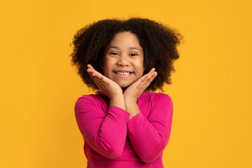 Portrait of overjoyed little black girl touching her face with excitement