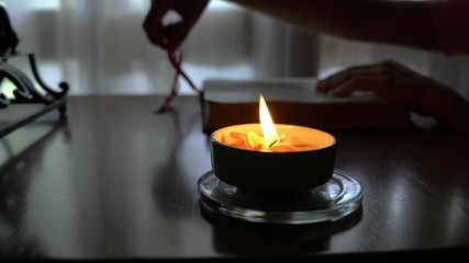 Burning candle on a table with a woman reading a book at the background