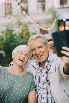 Senior man taking selfie with happy woman while sitting at restaurant in city