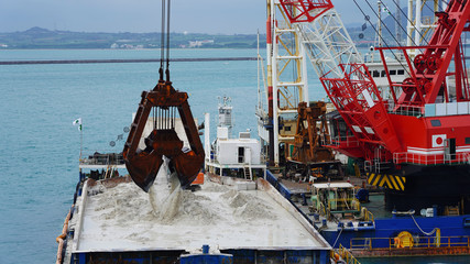 Huge excavator on floating platform in the blue water of the Pacific Ocean extract white sand from the bottom and load onto a barge amid clouds and tropical islands. close up crane basket plunge © Artem