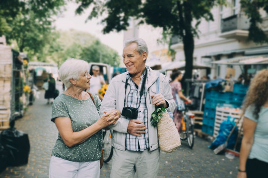Happy senior couple talking while walking arm in arm at street market