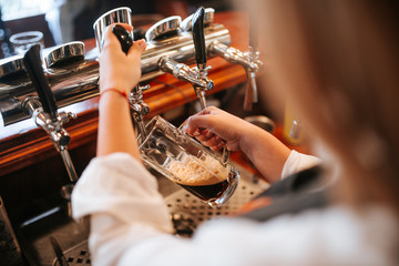 A young attractive blonde caucasian  waitress pouring beer in a cafe