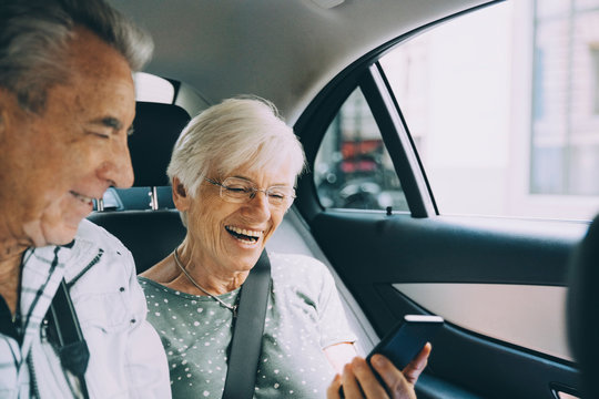 Smiling retired couple using mobile phone while sitting in car during vacation