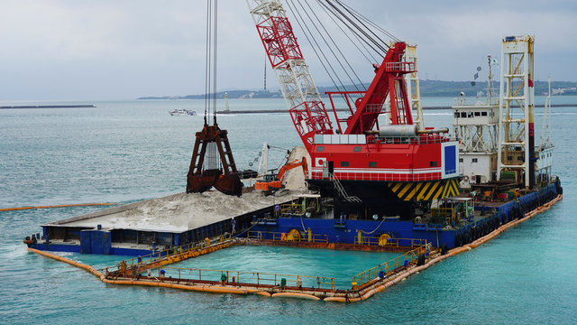 Floating crane platform with a huge bucket extracts sand from the bottom of the Pacific Ocean.
a huge crane extracts white sand from the ocean off the coast of Okinawa.