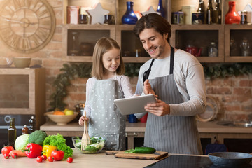 Recipe App. Father and little daughter using digital tablet in kitchen