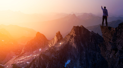 Adventurous Man Hiker With Hands Up on top of a Steep Rocky Cliff. Sunset or Sunrise. Composite. Landscape Taken from British Columbia, Canada. Concept: Adventure, Explore, Hike, Lifestyle