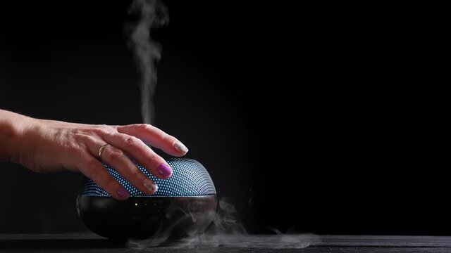 Woman add essential oil into Diffuser on black, closeup