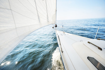 White yacht sailing on a sunny summer day. Top down view from the deck to the bow and sails. Waves...