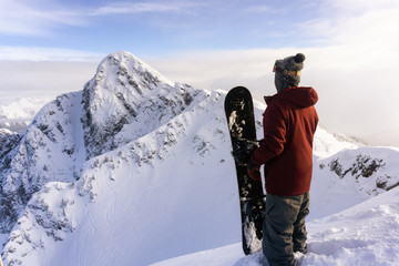 Snowboarder is standing on top of the mountain and looking at the beautiful scenery. Taken in Revelstoke Ski Resort, British Columbia, Canada. Adventure, holiday concept