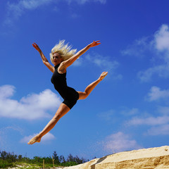 Fototapeta na wymiar beautiful blonde girl dancer jumping on the white sand. gymnast doing the splits in the air against a blue sky. freedom to jump in sunny weather. gymnastic split 