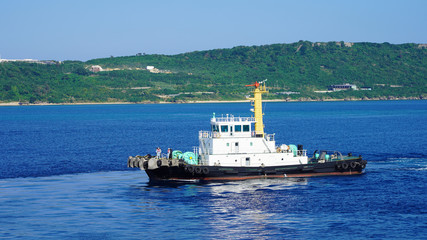 Colored tugboat works in port. bright tugboat in blue water. industrial ship on waves tropical...