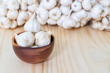 Garlic bulbs in wooden bowl on wooden table with garlics blur background..