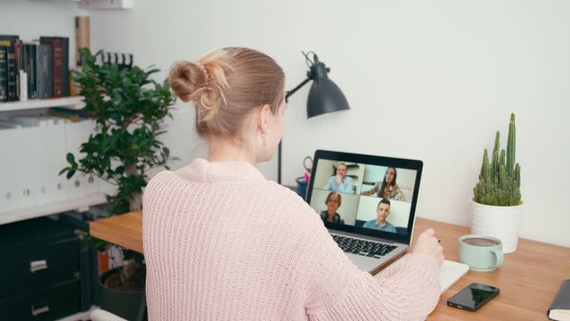 Woman Greets Work Team in Online Group Video Call Conference using Laptop in Home Office. Family or Collegues Talk via Internet. Self-isolation at COVID-19 Pandemic. 4K Medium Orbit Shot