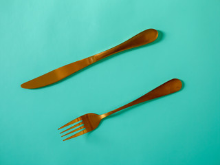 Yellow metal knife and fork imitating gold on a blue background