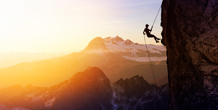 Composite. Silhouette Rappelling from Cliff. Beautiful aerial view of the mountains during a colorful and vibrant sunset or sunrise. Landscape taken in British Columbia, Canada. Concept: Adventure
