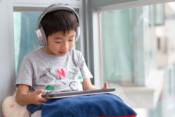 A boy is using digital tablet screen for playing game,doing homework in the house living room.Education school, technology learning  and computer concept.