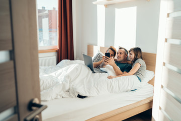 Family laying in bed and using smartphone