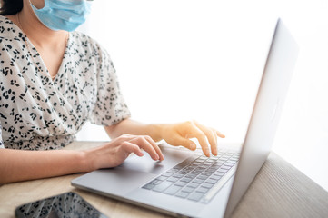 Close up low angle view of Woman in quarantine for Coronavirus wearing protective mask and smart working Hands holding credit card and using laptop. Online shopping