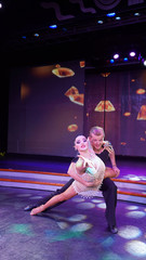 a pair of dancers dancing on stage in the light of colorful bright spotlights and smoke. support in classic ballroom dancing waltz, sensual couple. choreography