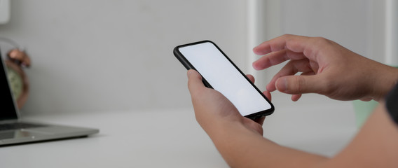 Cropped shot of male freelancer working on blank screen smartphone at minimal home office