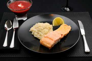 Black table setting with plate of salmon lemon and risotto with borscht soup