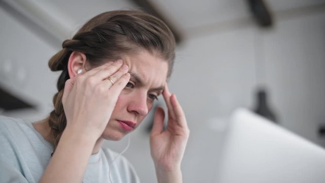 Young beautiful girl is working on a laptop. Strong headache. Massage of the temporal lobe. Upset student. Deep feelings of grief.