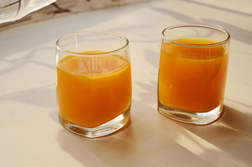 two glass glasses with buckthorn juice on a sunny window sill with shadows