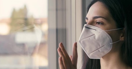 Authentic portrait of an young woman wearing a protective mask is looking through a window. Concept of pollution, environment, protection, virus transmission, breathing,safety, quarantine, covid-19 - Powered by Adobe