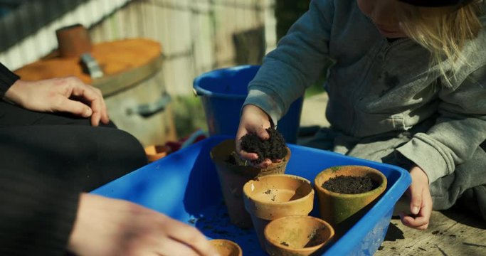 Young mother helping her preschooler plant seeds in plant pots