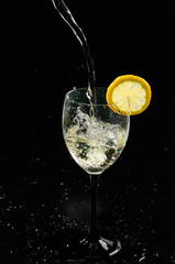 Pouring white wine into a glass with a lemon slice on black background
