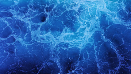 Close-up on blue ocean water on a sunny day, foaming water, sea texture, view from the deck of a ship