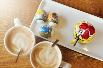 Happy Easter holiday in a cafe, two white cups of coffee on a wooden table, a white plate with colored eggs