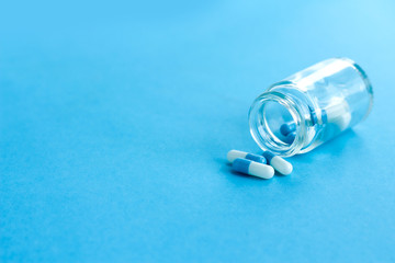 Prescription drugs cascade from a transparent pharmacy bottle, on a blue background.