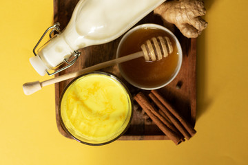 Turmeric milk and the ingredients for making the drink are on a wooden tray. Yellow background and top view. Natural light and shade