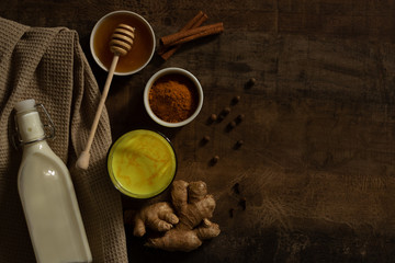 Turmeric Milk is poured into a glass. Next to it are the ingredients for making a drink - milk in a bottle on a napkin, spices and honey.  Top view