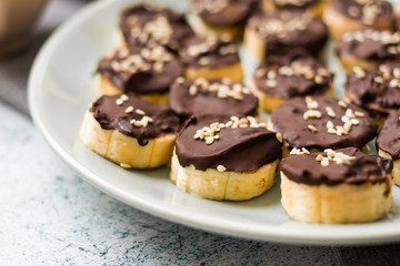 Banana slices in melted chocolate with sesame seeds. Vegan sweet healthy dessert.