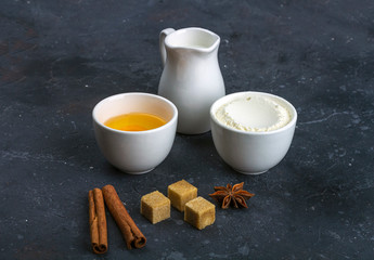 Baking background. Ingredients for cooking cake (flour, egg, milk, anise, cinnamon, cane sugar) in bowls on dark table. Food concept. Close up layout, copy space for text.