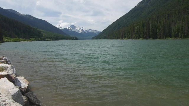 Static shot looking out over Duffey Lake from the vewpoint during the summer with clear skys and a snow topped mountain in the background