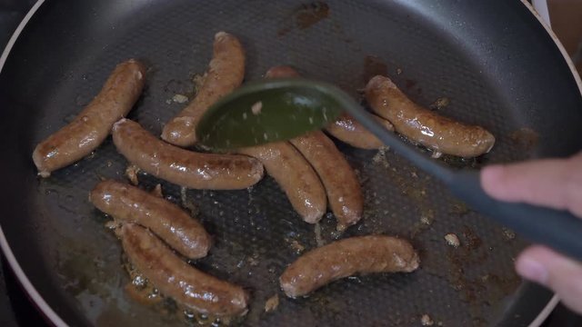 Slow motion of Grill Tongs flipping Sausages on a sizzling hot grill plate